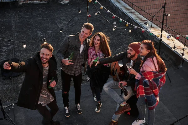 Samimi duygular. Dekoratif renkli ampullerle çatıda eğlenirken selfie çeken genç bir arkadaşın en iyi görüntüsü..