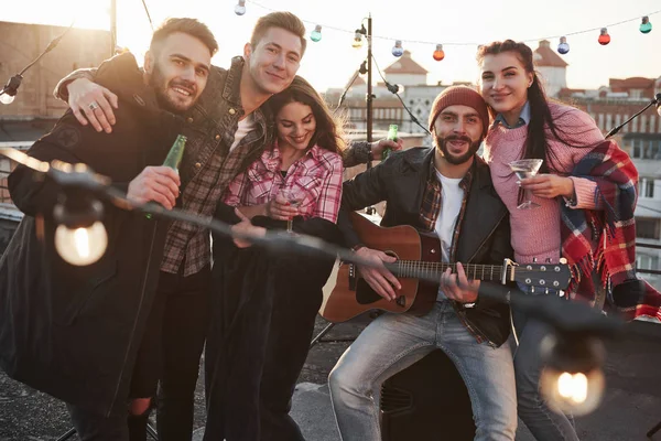 Çatıda parti var. Alkol ve gitarla fotoğraf için poz veren beş yakışıklı arkadaş..