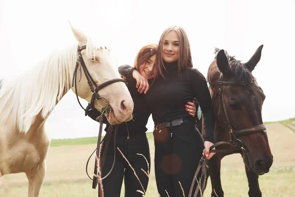 Two young beautiful girls in gear for riding near their horses. They love animals.