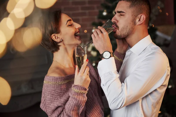 男人在女朋友笑的时候喝香槟 一对漂亮的夫妇穿着经典漂亮的衣服在屋里庆祝新年 — 图库照片