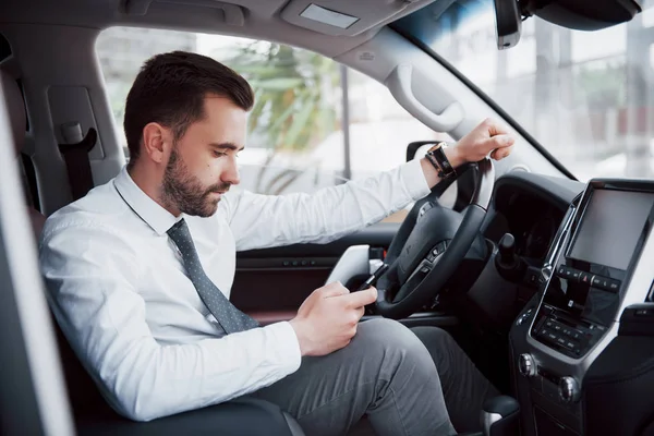 車を運転しながら携帯電話を見て満足した若いビジネスマン — ストック写真