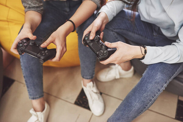 Twin sister sisters play on the console. Girls hold joysticks in their hands and have fun.