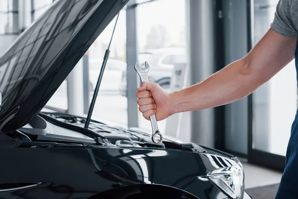 The hand of a car mechanic with a wrench in a combi zone near the car in the workshop