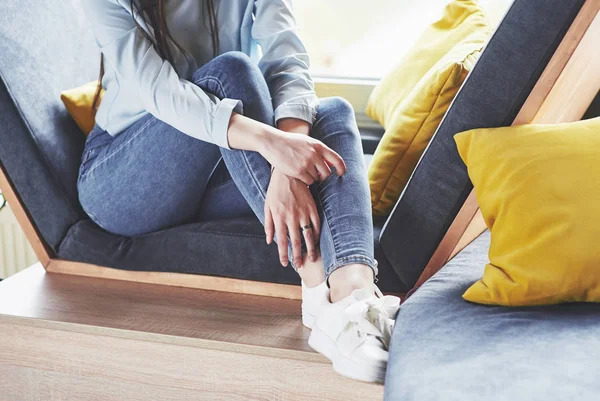 Beautiful young girl spends her time in the recreation area. She sits and has fun in the sofa chair in the form of a hexagon with pillows near the window. Conceptual cropping