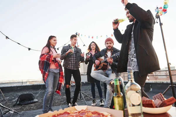 Enjoying the song. Table with food. Weekend on the rooftop with guitar, alcohol and pizza.