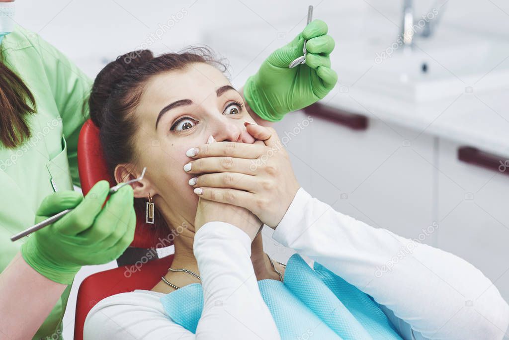 Frightened girl at dentist office covered mouth with hands. Concept phobia dental office.