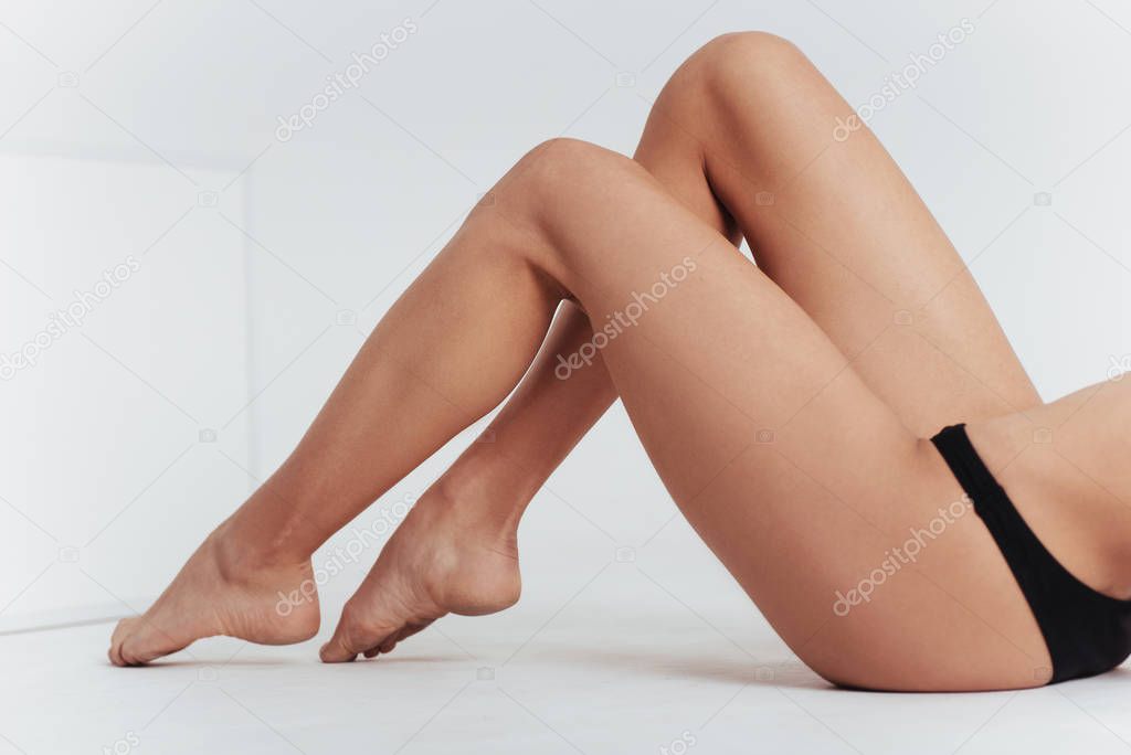 Cropped image of girl in black underwear lying down on the white floor.