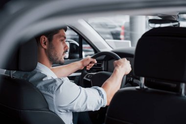 Genç bir adam yeni alınmış bir arabada oturuyor ve ellerini dümene koyuyor.