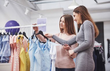 Yeni elbiselere bakmalıyız. Alışveriş çantalı iki güzel kadının, mağazada yürürken gülümseyerek bakışlarına bakmalıyız..