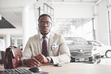 Çekici siyah işadamı araba galerisinde masaya oturur, bir sözleşme imzalar ve yeni bir araba alır..