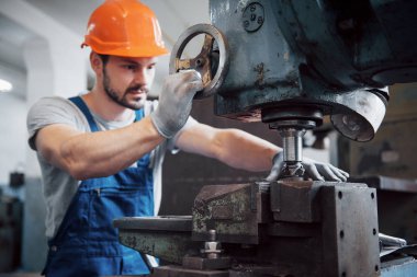 Büyük bir metal fabrikasında kasketli genç bir işçinin portresi. Makinelere hizmet eden mühendis, gaz ekipmanları için parça üretiyor..