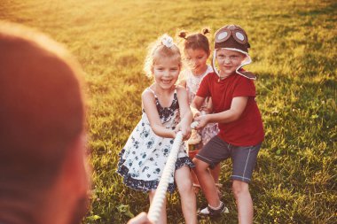 Çocuklar parkta babalarıyla oynuyorlar. İpi çekerler ve güneşli bir günde uzanarak eğlenirler..