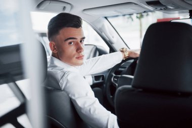 Genç bir adam yeni alınmış bir arabada oturuyor, başarılı bir satın alma.