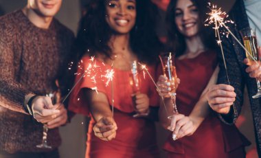 Çok ırklı arkadaşlar yeni yılı kutluyor. Bengal ışıkları ve bardaklarla içki içiyorlar..
