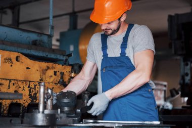 Büyük bir metal fabrikasında kasketli genç bir işçinin portresi. Makinelere hizmet eden mühendis, gaz ekipmanları için parça üretiyor..