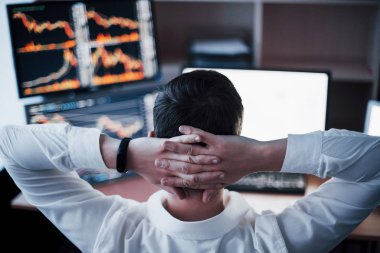 Yeni yaklaşımlar geliştiriyoruz. Gelişigüzel giyinen, kafasının arkasından el ele tutuşan ve yaratıcı ofisteki masada otururken çalışan genç adamın arka görünüşü..