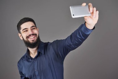 Mutlu gülümseyen yakışıklı sakallı genç adam selfie çekiyor..