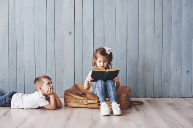 Büyük seyahate hazırız. Küçük mutlu kız ve çocuk ilginç bir kitap okuyor büyük bir evrak çantası taşıyor ve gülümsüyor. Seyahat, özgürlük ve hayal gücü kavramı.
