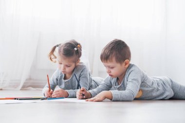 Çocuklar pijamalarıyla yere yatar ve kalemle çizerler. Kalemlerle resim yapan şirin bir çocuk..