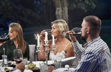 Şarabı eleştirirken. Yetişkin arkadaşlar akşam vakti restoranın arka bahçesinde dinlenip sohbet ediyorlar..