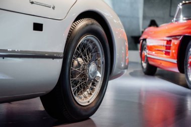 Arka planda kırmızı araba olan nadir bulunan beyaz aracın arka tekerleğine odaklan..