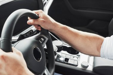 Genç bir adam yeni alınmış bir arabada oturuyor ve ellerini dümene koyuyor.