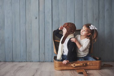 Pilot şapkalı mutlu çocuk ve eski bavulla oynayan küçük kız. Çocukluk. Hayal gücü, hayal gücü. Seyahat kavramı.