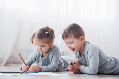 Çocuklar pijamalarıyla yere yatar ve kalemle çizerler. Kalemlerle resim yapan şirin bir çocuk..
