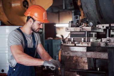 Büyük bir metal fabrikasında kasketli genç bir işçinin portresi. Makinelere hizmet eden mühendis, gaz ekipmanları için parça üretiyor..