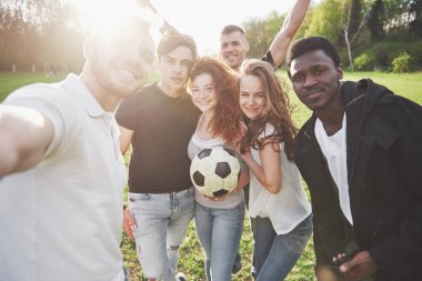 Gündelik kıyafetli bir grup arkadaş futbol sahasında sefi yapıyor. İnsanlar eğleniyor ve eğleniyor. Aktif dinlenme ve manzaralı gün batımı.