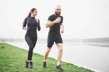 Couple jogging and running outdoors in park near the water. Young bearded man and woman exercising together in morning.