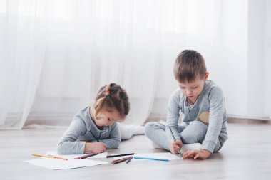 Çocuklar pijamalarıyla yere yatar ve kalemle çizerler. Kalemlerle resim yapan şirin bir çocuk..
