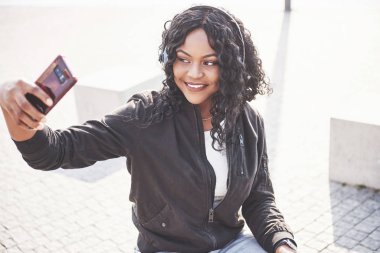 Sahilde ya da gölde oturan ve kulaklıklarıyla müzik dinleyen güzel bir Afrikalı Amerikalı kızın portresi..