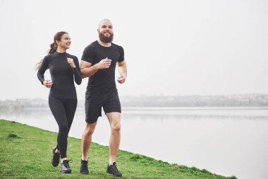 Couple jogging and running outdoors in park near the water. Young bearded man and woman exercising together in morning.