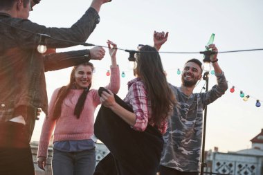 Akılda kalıcı bir şarkı. Bunu jestlerinden anlayabilirsin. Arka planda güzel güneş ışığı olan çatıda dans partisi. Genç şık insanlar..