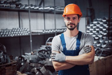 Büyük bir metal fabrikasında kasketli genç bir işçinin portresi. Shiftman bitmiş ürünlerin deposunda..