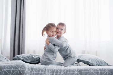 Beyaz yatak odasında oynayan mutlu çocuklar. Küçük çocuk ve kız kardeşi ve kız kardeşi pijama giymiş yatağa oynamak. Çocuklar için kreş iç. Kıyafeti ve yatak takımları bebek ve yürümeye başlayan çocuk için. Aile evde.