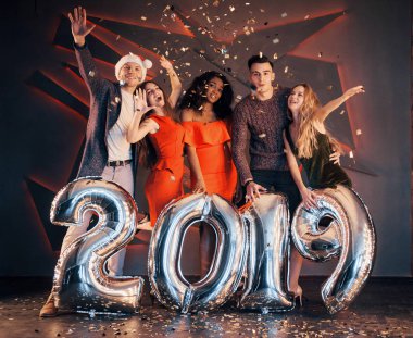 Yeni 2019 yaklaşıyor. Noel Baba 'nın şapkasıyla bir grup mutlu genç ve çok uluslu insan, üzerinde gümüş rakamlar olan ve partide konfeti atan. Mutlu yıllar.
