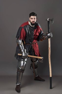 Gri arka planda ortaçağ şövalyesi. Zincirli zırhlı, kırmızı, siyah elbiseli ve savaş baltalı zalim, kirli yüzlü bir savaşçı portresi..