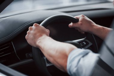 Genç bir adam yeni alınmış bir arabada oturuyor ve ellerini dümene koyuyor.