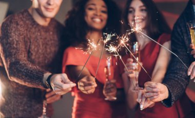 Yılbaşı kavramı. Çok ırklı arkadaşlar yeni yılı kutluyor. Bengal ışıkları ve bardaklarla içki içiyorlar..