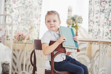 Şirin küçük çocuk ilk kez okula gidiyor. Okul çantası ve kitabı olan bir çocuk. Çocuk evrak çantası yapıyor, arka planda çocuk odası. Okula geri dön..