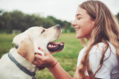 Parkta yeşil çimlerin üzerinde güzel bir köpeği olan güzel bir kızı çerçevelet.
