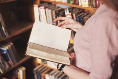 Genç çekici kütüphaneci kütüphane rafları arasında kitap okuyor..