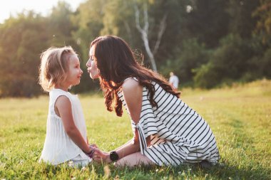 Mutlu anne ve kız güneşin altında bir parkta sarılıyorlar. Parlak bir yaz otlarının arka planında.