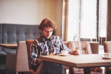 Sıcak bir kafe sahibi olan mutlu adam yemek masasında dokunmatik bir şekilde otururken kendi başarısının keyfini çıkarıyor. Elinde dijital tabletle gülümseyen bir erkek kahve dükkanında yemek yerken güzel şeyler düşünüyor..