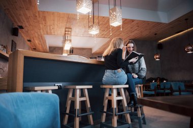 Kafe molasında kitap okumaya dalmış iki kız. Sevimli genç bayanlar kitap okuyor ve kahve içiyorlar..