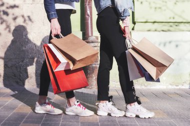 Two young woman carrying shopping bags while walking in the street after visiting the stores.