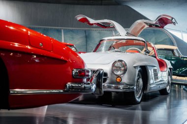 Kapılar ardına kadar açılıyor. Otomobil fuarında siyah fayansların önünde duran klasik arabalar.