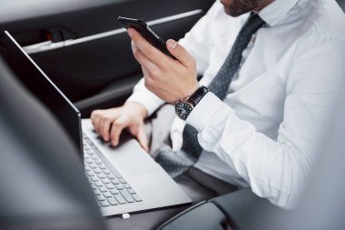 Genç bir iş adamı dizüstü bilgisayarda çalışıyor ve arabanın arkasında otururken telefonla konuşuyor. Hareket halinde çalışır, zamanını takdir eder..